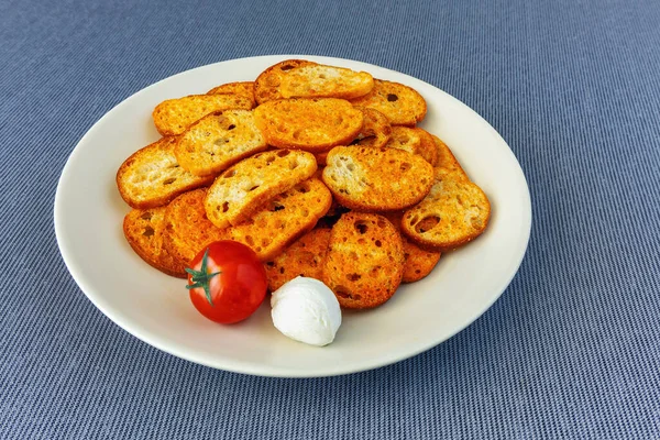 灰色の布のテーブルクロスに皿の上にトマトとモッツァレラチーズの風味のトーストパンのスライス — ストック写真
