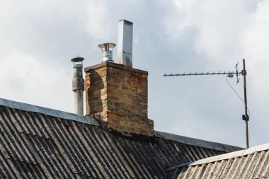 Eski tuğladan bir evin bacası, tahta tavanına metal eklenmiş ve TV anteni var.