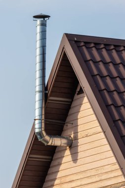 Güneşli bir günde evin yan tarafındaki metal baca gökyüzünün arka planına karşı.