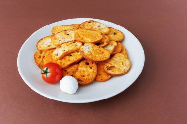 Kahverengi arka planda bir tabakta domates ve mozarella aromalı kızarmış ekmek dilimleri.