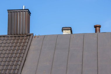 Yuvarlak paslanmaz metali olan evin bacası teneke çatının üzerine yerleştirilmiş, gökyüzü arka planlı.