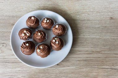 Ev yapımı mini çikolatalı kekler, tabakta süslemeler, meşe masa yüzeyi, üst manzara.