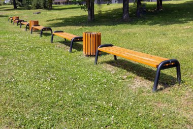 Yaz boyunca, güneşli bir günde, dinlenmek için çayır üzerinde çöp tenekeleri olan banklar var.