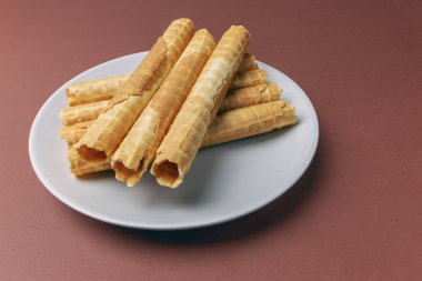 Kahverengi arka planda gri bir tabakta taze tereyağlı waffle tüpleri.