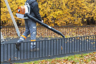 Sonbaharda, hava yastıklı bir kamu görevlisi şehir parkındaki bir oyun alanından yaprakları üflüyor.