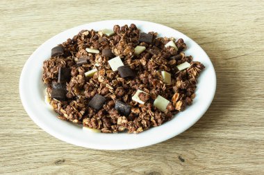 Yulaf ezmeli granola ve meşe ağacının üzerinde beyaz bir tabakta çikolata parçacıkları.