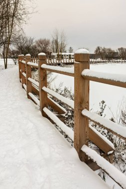 Kışın, gölün etrafında parmaklıklar olan tahta bir tahta kaldırım, parkta karla kaplıdır.