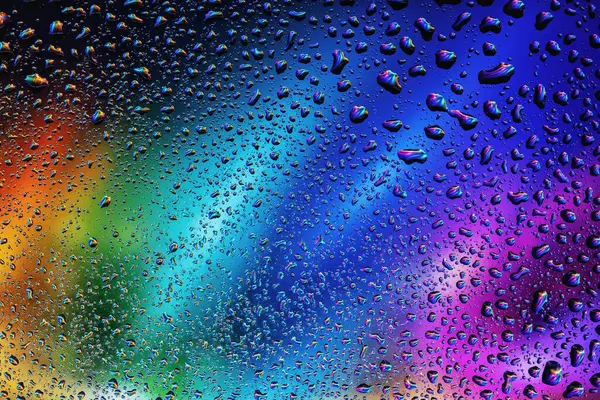 Close-up view of raindrops on a glass surface with a blurred background in shades of purple and blue, creating an abstract and serene atmosphere.