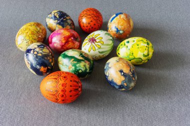 Çok güzel dekore edilmiş Paskalya yumurtalarının çeşitli canlı renklerde, kumaştan gri bir masa örtüsü üzerinde düzenlenmiş, bayram sezonu için neşeli ve neşeli bir bahar atmosferini çağrıştıran tepeden aşağı bir görüntüsü..