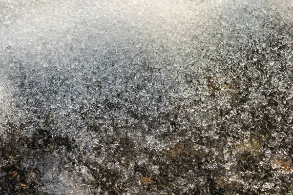Siyah asfalt üzerinde eriyen karın makro görüntüsü, baharın gelişini ve kış karının erimesini simgeliyor.