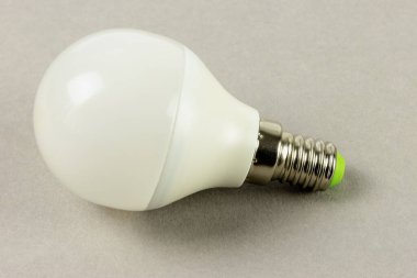 Beyaz LED ampul nötr gri bir arka plana yerleştirilir, opak kapağı ve metal vida tabanı modern enerji tasarrufu teknolojisini yansıtır.