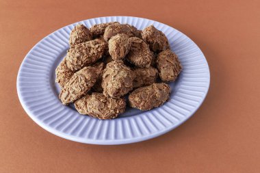 Belgian chocolate truffles covered with milk chocolate chips on a plate on a brown background, front view clipart