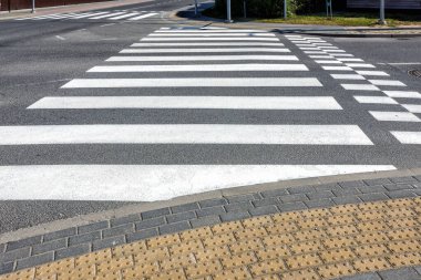 Asfalt bir caddede yeni boyanmış beyaz çizgilerle karşıdan karşıya geçmek. Ön taraftaki kavşakta görme engelliler için dokunsal bir kaplama var..