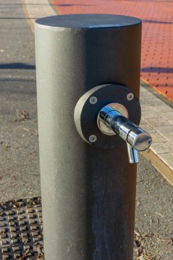 Gündüz vakti şehir parkında optik musluğu olan modern bir su sütunu.