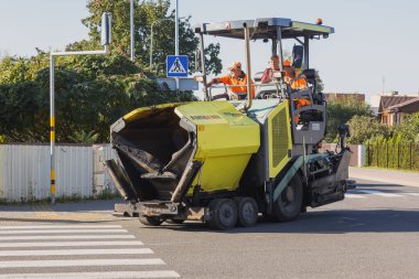Büyük sarı bir endüstriyel yol yapım makinesi şehir sokaklarına taze asfalt seriyor. Panevezy 'ler. Litvanya. 08 numara. 07 numara. 2023.