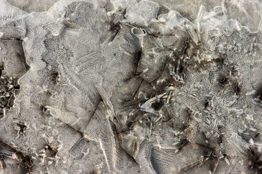 Donmuş buz yüzeyinin arka planında karmaşık çatlaklar ve hava kabarcıkları ortaya çıkıyor. Buz çeşitli desenler sergiler.