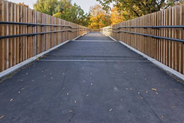 Huzurlu bir patika, ahşap çitlerle ve canlı sonbahar yeşillikleriyle kaplı, sonbaharda parkta sakin yürüyüşlere davetiye çıkarıyor..
