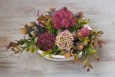 Kurutulmuş Echinops setifer ve Eryngium bourgatii 'nin eski ahşap bir zeminde seramik bir kasede yerleştirilmesi.