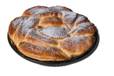 Süzme peynirli yumuşak ve pofuduk kek, siyah bir fırın tepsisinde oturur. Pasta toz şekere bulanır, altın rengi ve davetkar dokusu sergilenir..