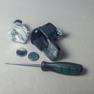 Açık mercek, pil ve tornavida içeren düz bir yüzeye yerleştirilen bisiklet hafif parçaları, bakım veya kurulum görevlerine hazırlık niteliğindedir..