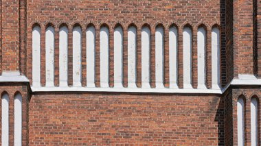 Güneş ışığı tarihi bir binanın dekoratif tuğla işçiliğini aydınlatır. Duvarcılığın zengin kırmızı tonlarına karşı dikey beyaz aksanları vurgular..
