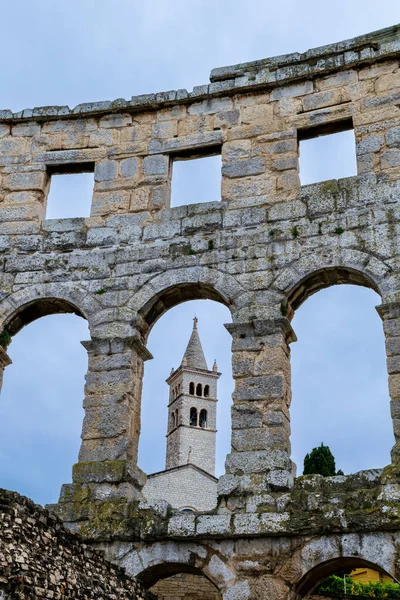 Antik amfitiyatroyla Pula 'da bir araya gelme ve kemerden geçen yeni bir kilise kulesi.