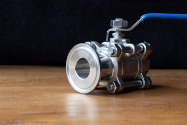 Three-piece ball valve, a flow control device which controls fluid flowing through it. On a wooden table, copy space to left.