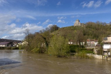 View of a swollen River Meuse at Dun-sur-Meuse, in the Meuse Valley in France. The church of Our Lady is visible in it's prominent hill top location. clipart