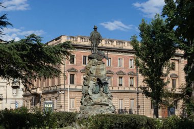 AOSTA, ITALY, 2 AĞUSTOS 2024: Kamu parkının manzarası, Aosta şehrinde ağaçlar ve eski bronz heykellerle Emilio Lussu. Aosta, Aosta Vadisi 'nde popüler bir turizm merkezidir. Yukarıdaki alanı kopyala.