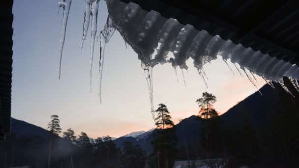 接近中だ 夕方には山の風景の背景に屋根の端に冷凍つらら 冬時間だ スローモーション — ストック動画
