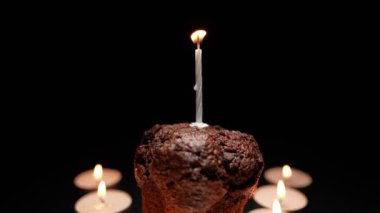 Chocolate muffin with a burning candle on a black background. Concept of memorial services and religion.