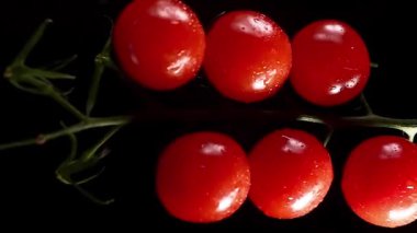 Vertical Video, Red Cherry Tomatoes Rotate on a Black Background. Juicy Vegetables in Water Drops. Vegetarian Concept. Slow Motion.