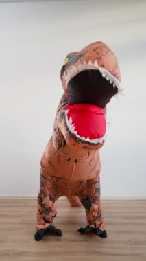 Vertical video, Happy Man in a Funny Dinosaur Costume is Dancing on a White Background. Slow Motion.