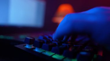 Close-up, Unrecognizable Man Using a Computer Keyboard to Code a Website in Neon Lighting. Hacker and Cybercrime or Cyberspace Concept. 