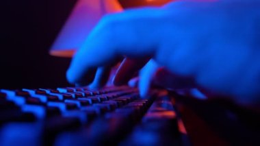 Male Hands Typing on a Computer Keyboard in Neon Lighting. Unrecognizable Guy Working on a Laptop at Night. Concept of Hackers and Cyber Crimes or Cyberspace.