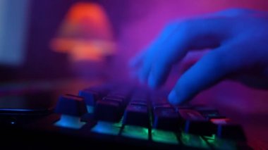 Male Hands Rapidly Typing on a Computer Keyboard in Smoky Neon Lighting. Unrecognizable Guy Working on a Laptop at Night. Concept of Hackers and Cyber Crimes or Cyberspace.