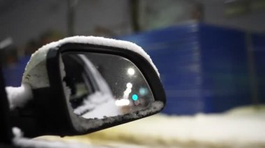 View from inside the car on the side mirror driving on a winter city road during a snowfall at night. Slow motion.