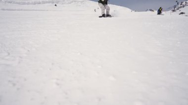 ELBRUS, RUSSIA - FEBRUARY 25, 2023: Snowboarder slows down on a snowboard raking snow into the camera super slow motion.