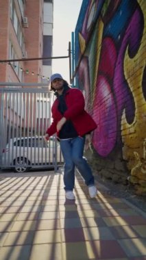 Dikey Video, Sokak Dansçısı Kırmızı Ceketle Modern Hip Hop Dansı Yapıyor. Tarz sahibi adam Günışığında Modern Koreografi sergiliyor. Yeraltı Atmosferi.