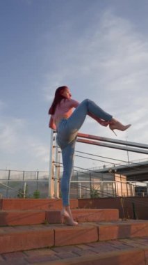 Vertiocal Video, Kot Giyen Zarif Kadın ve Yüksek Topuklar Bacağını Gün Batımında Ayırıyor. Havalı esnek bacaklı atletik zayıf kız bacağını harika kaldırıyor. Yavaş Hareket.