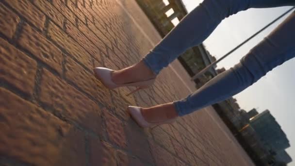 ハイヒールとジーンズのビジネスウーマンは サンセットライトのシティパークを歩いています 美しいスリム女性の足は 日光のタイルシティストリートを歩く 認識できない人 スローモーション — ストック動画