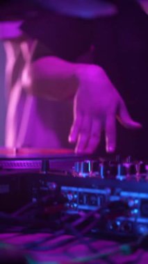 Dikey video, DJ gece kulübü partisinde DJ konsol açık renk müzik parçalarını karıştırıyor. Gece kulübü disko partisinde DJ Mixer Controller masası. Eller düğmelere basıyor ve sürgüler Elektronik Müzik Çalıyor