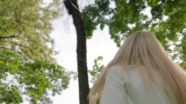 Güneşli bir günde Şehir Parkı 'nda Dönen ve Gülümseyen Mutlu Sarışın Kadın. Beyaz ceketli ve Fuchsia etekli güzel kız dışarıda eğlenirken özgürlüğü ve mutluluğu hissediyor. Yavaş Hareket