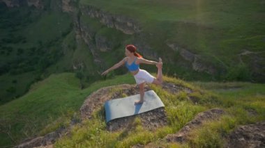Güneş batarken bir dağın tepesinde yoga yapan atletik kadın. Spor Kız Eğitimi ve Dağlarda Esneme Egzersizleri Yapıyor. Sağlıklı Yaşam Tarzı, Zenizm, Spor Konsepti. Yavaş Hareket.