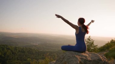 Güneş batarken bir dağın tepesinde yoga yapan atletik kadın. Spor Kız Eğitimi ve Dağlarda Esneme Egzersizleri Yapıyor. Sağlıklı Yaşam Tarzı, Zenizm, Spor Konsepti. Yavaş Hareket.