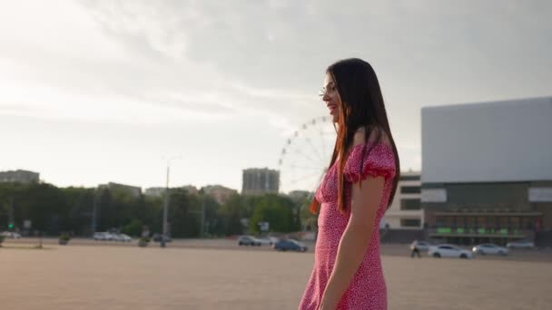 ピンクのドレスとメガネで魅力的なブルネットの女性 シティセンターで笑顔とウォークス ハッピーガールは街で散歩を楽しんでいる スローモーション — ストック動画