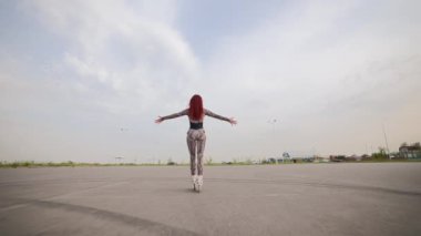 Kızıl saçlı sıska kadın asfalt bir otoparkta paten kayarken eğleniyor. Happy Girl Paten Yapıyor ve Kollarını Yanlara Kaldırıyor, Özgürlüğü ve Refahı Hissediyor. Yavaş Hareket.