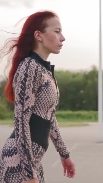 垂直录像 一头红头发的瘦女人在一个沥青停车场上翻滚 快乐女孩轮滑和举起她的胳膊 感受自由和幸福 慢动作 — 图库视频影像