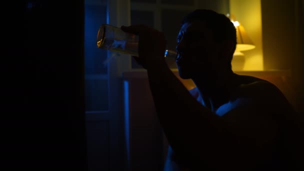 一个沮丧的人在黑暗中喝着玻璃瓶中的酒精的轮廓 酗酒和吸毒成瘾的问题 慢动作 — 图库视频影像