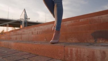 Yüksek Topuklu Ayakkabılı İnce Kadın Bacakları Şehir Parkı 'nda Günbatımı Işığında Yürüyor. Gün batımında Güzel Bacaklı Kadın Merdivenlerden Aşağı Gidiyor. Tanınmayan kişi. Yavaş Hareket.